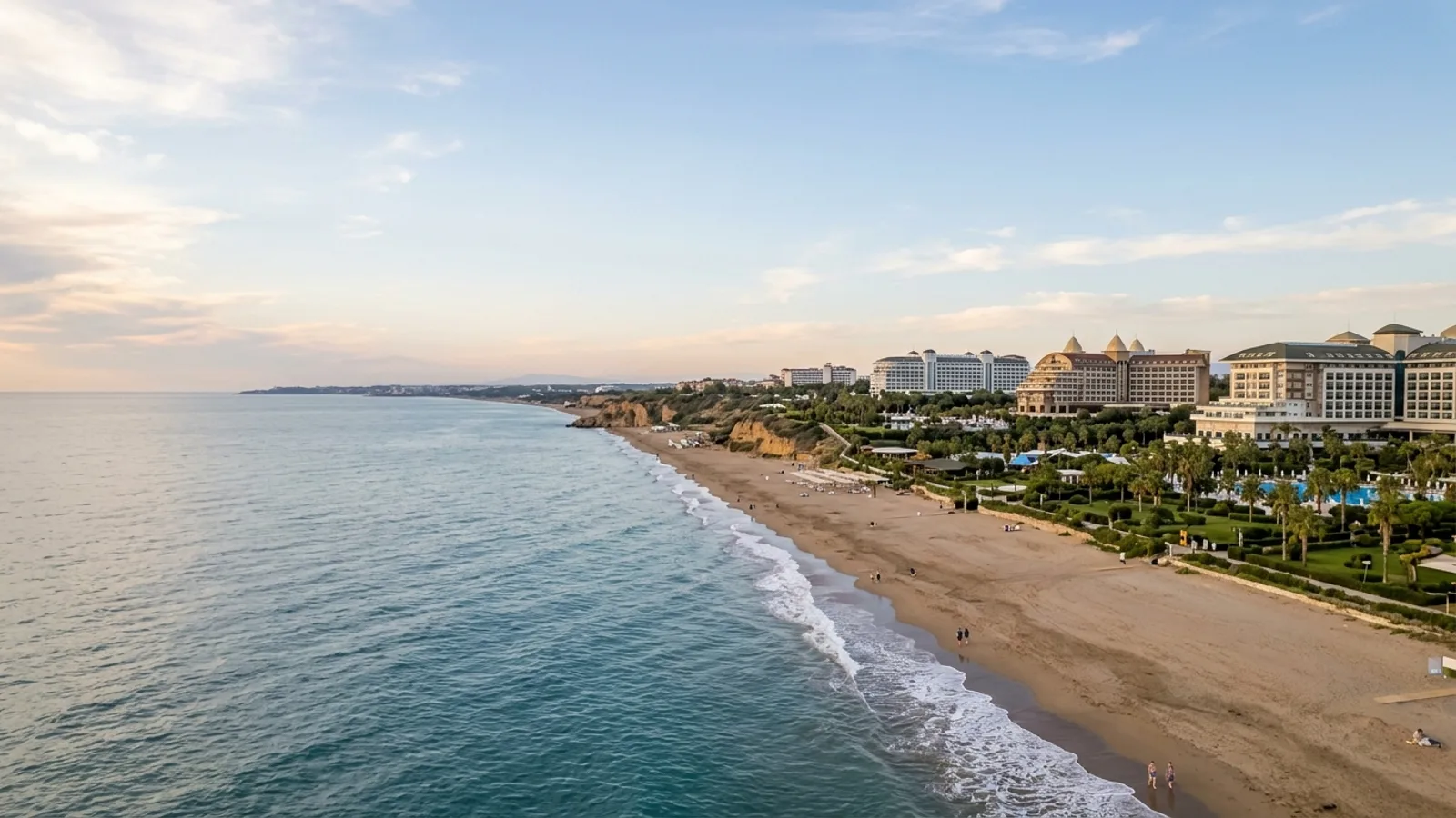 Lara, Türkiye — the long straight sandy beach at Lara east of Antalya, with low cliffs behind the shore and large resort hotels set back among landscaped gardens.