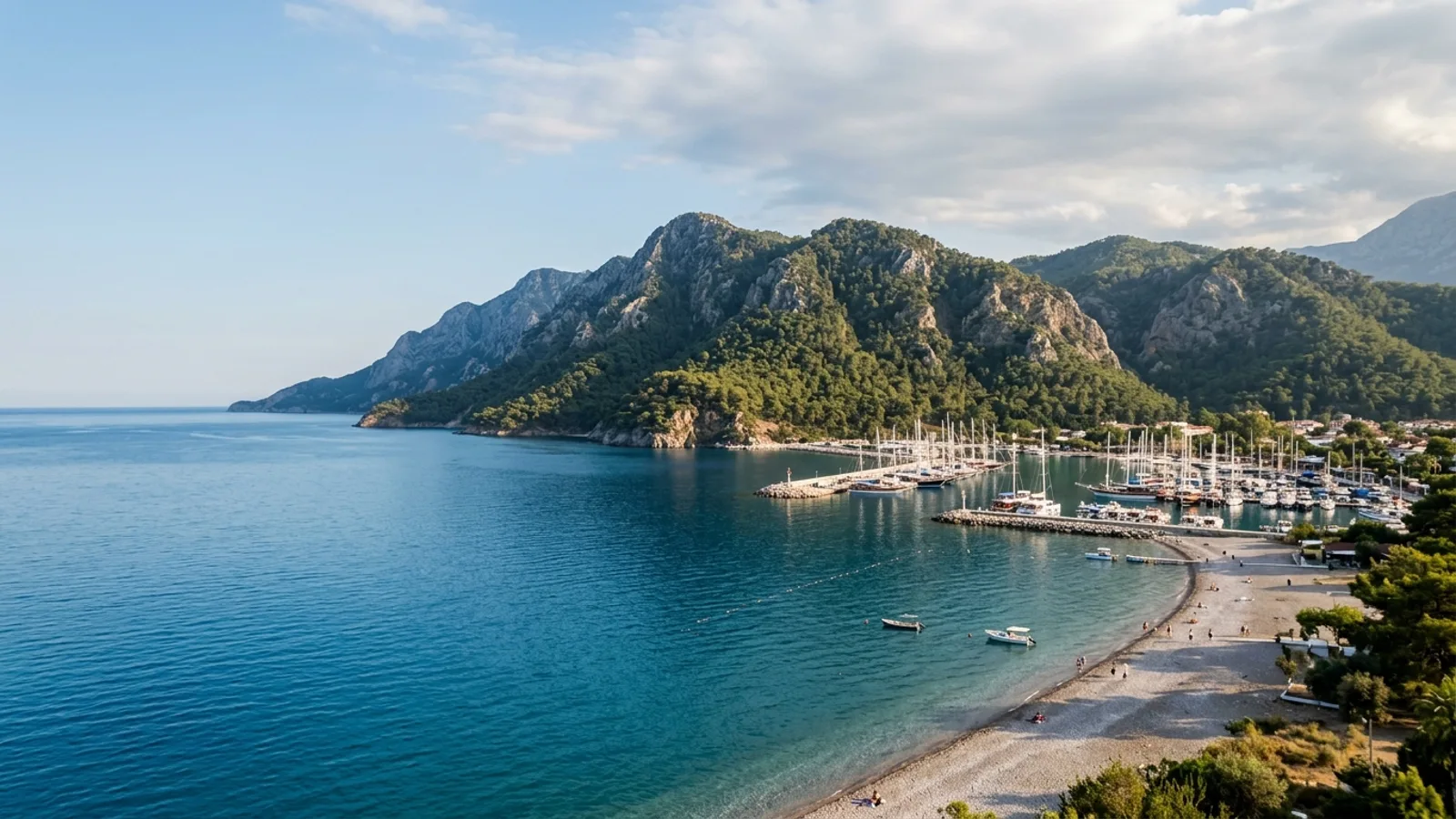 Kemer, Türkiye — the coast at Kemer, a pebble beach and yacht marina where pine-covered Taurus mountains drop almost vertically into a deep blue sea.