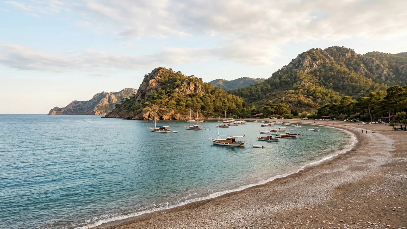 Adrasan, Türkiye — the sheltered bay at Adrasan, a crescent pebble beach with fishing boats moored offshore and pine-covered headlands on both sides.