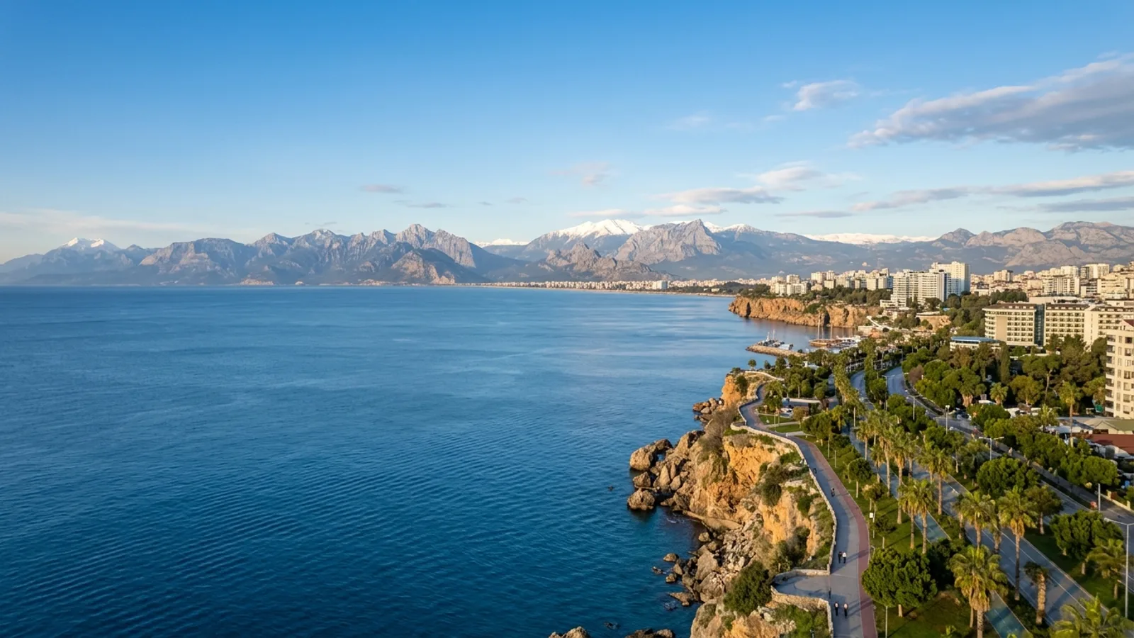 Antalya City Centrum, Türkiye — the modern seafront of Antalya city, palm-lined boulevards on the cliff top and the snow-topped Taurus mountains rising across the bay.