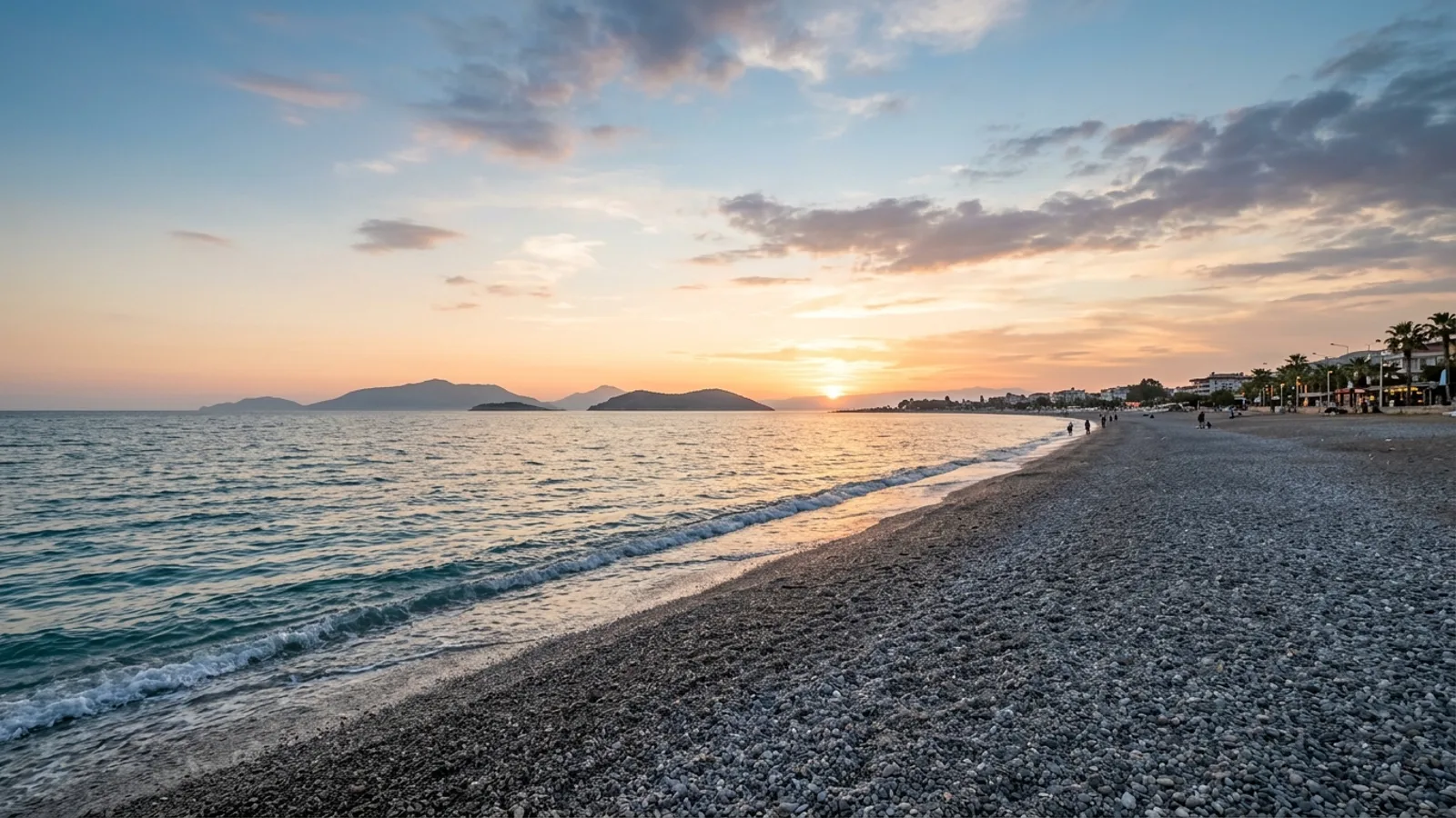 Calis Beach, Türkiye — the long straight pebble beach at Calis near Fethiye, a flat shore facing west across the bay towards low islands at sunset.