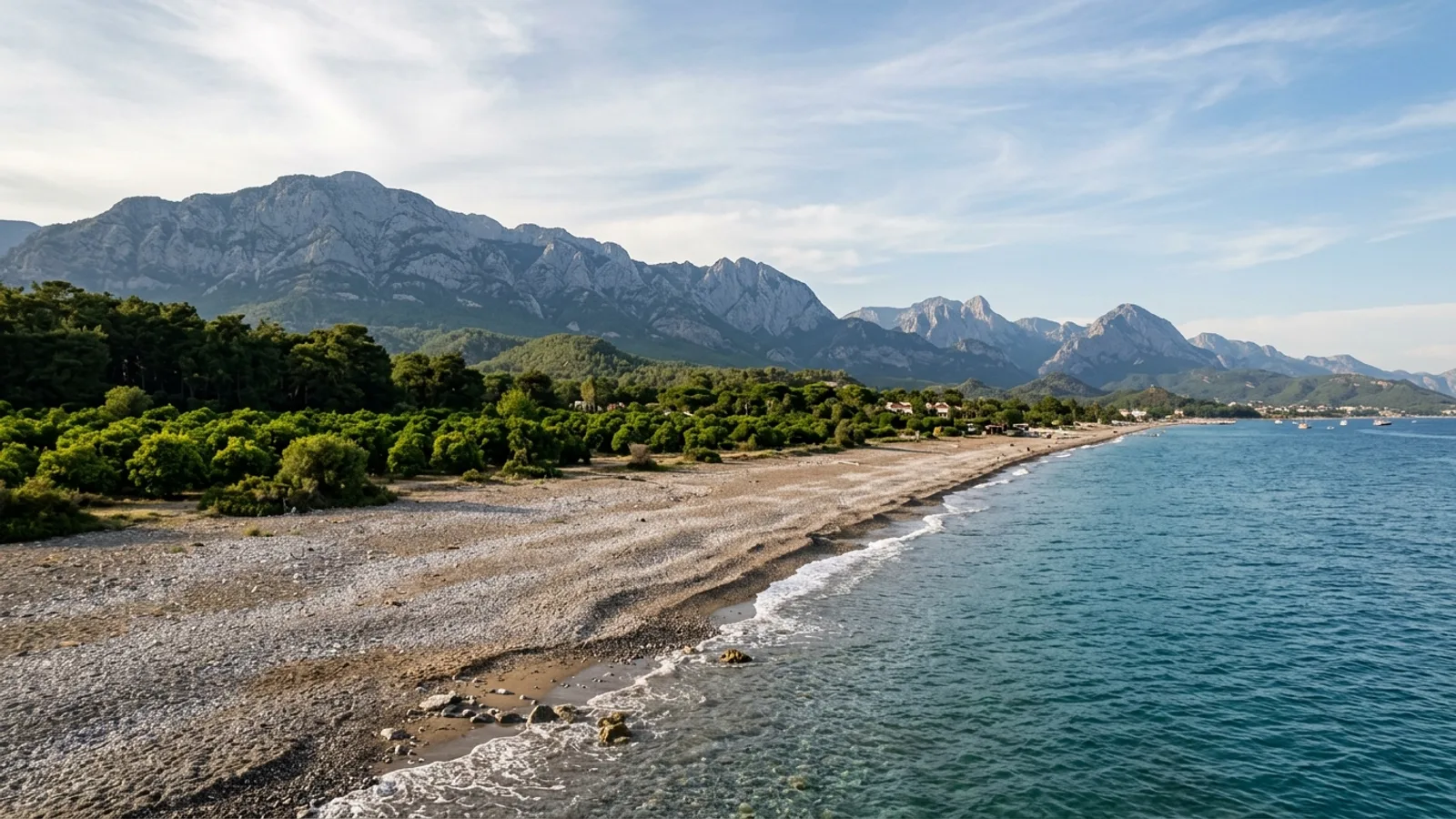 Camyuva, Türkiye — the pebble shore at Camyuva south of Kemer, orange groves and pine woods between the beach and the mountain wall behind.