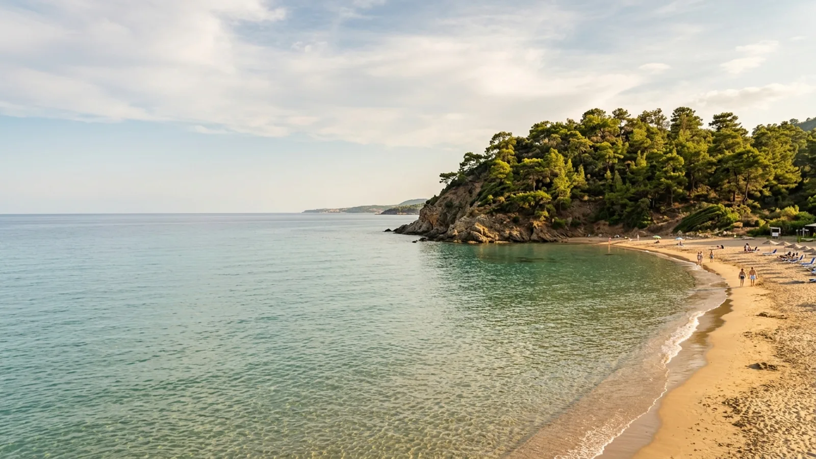Incekum, Türkiye — the shore at Incekum west of Alanya, a small sandy cove with very shallow clear water and a pine-covered headland to one side.