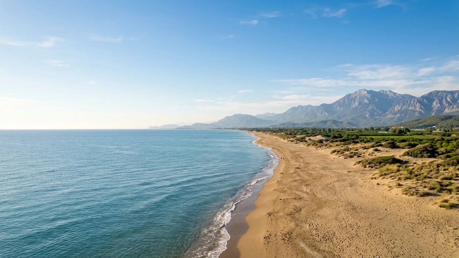 Kizilot, Türkiye — the long open sandy beach at Kizilot on the Antalya coast, low dunes and a flat green hinterland with distant mountains.