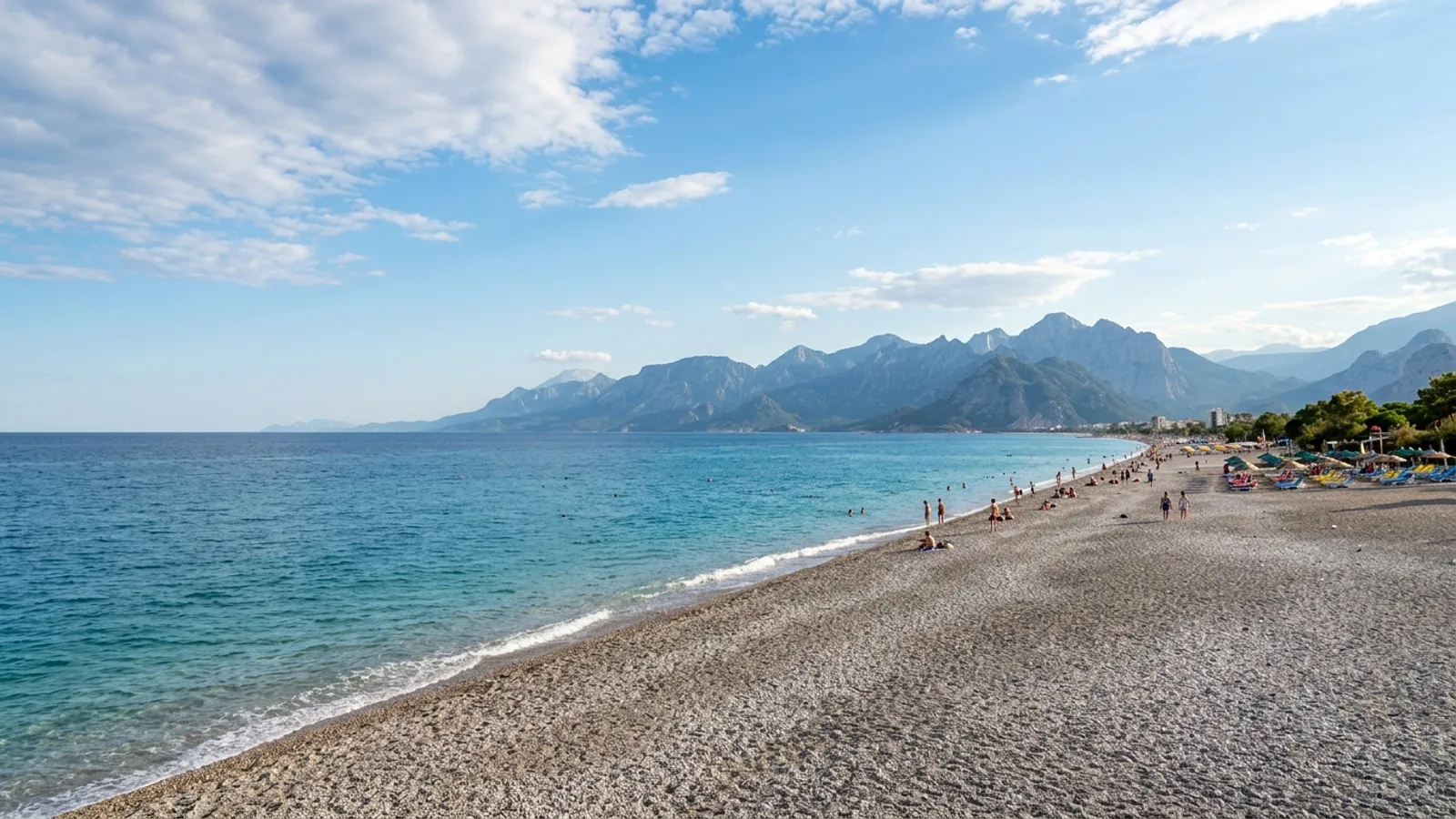 Konyaalti, Türkiye — Konyaalti beach in Antalya, a long grey pebble shore on a clear turquoise bay with the steep Beydaglari mountains rising straight from the water at the far end.
