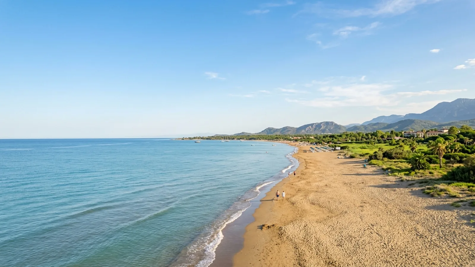 Kumkoy, Türkiye — the wide sandy beach at Kumkoy west of Side, calm shallow sea and a flat green coastal strip behind the shore.