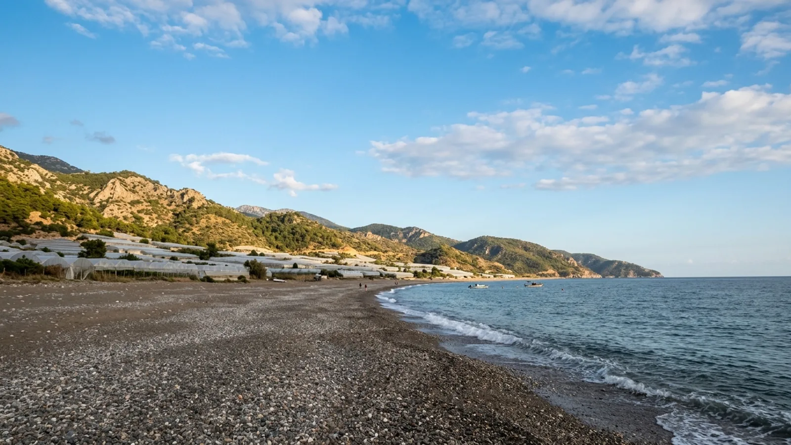 Mavikent, Türkiye — the shore at Mavikent on the coast south of Kumluca, a long quiet pebble beach with greenhouses and hills behind it.