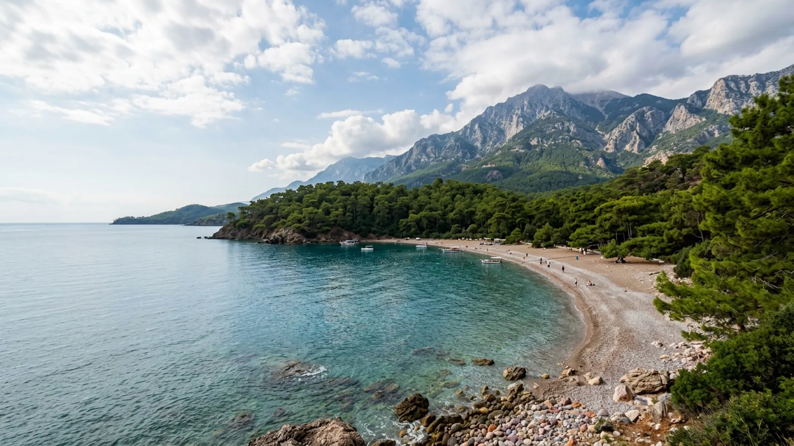Tekirova, Türkiye — the coast at Tekirova, a sheltered pebble bay ringed by dense pine forest with the high Taurus ridge behind.